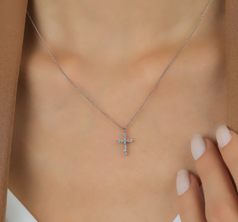 K&ouml;nnte beinhalten: Eine zarte Silberkette mit einem kleinen Kreuzanh&auml;nger, der mit funkelnden Edelsteinen besetzt ist. Das Kreuz ist an einer feinen Kette befestigt und erzeugt ein schlichtes, aber elegantes Design.