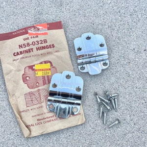 Peut inclure: Deux charnières de cabinet argentées avec des vis sur une surface en béton gris. Les charnières sont étiquetées "N58-032B Cabinet Hinges" et "Bright Chromium Plated with White Lines". Le prix est indiqué comme "Sale Price 1.69".