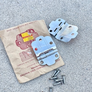 May include: Two silver-toned door hinges with a brown paper bag with the text "BRIGHT CHROMIUM PLATED WITH WHITE LINES" and "SALE PRICE 169" and "COMPLETE WITH SCREWS" and "ILLUSTRATION IS THE" and "MANUFACTURE NATIONAL LOCK COMPANY, ILLINOIS". A pile of silver screws are scattered on a grey concrete surface.