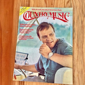 May include: A vintage magazine cover featuring a photo of country music singer Eddy Arnold. The cover is titled "Country Music" and features the text "Eddy Arnold, the Ideal American Male" and "August 1974, 75 cents".