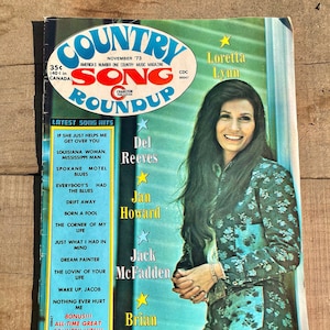 May include: A vintage magazine cover featuring a photo of Loretta Lynn, a country music singer. The cover is for the November 1973 issue of Country Song Roundup magazine. The cover features a list of the latest song hits, including songs by Del Reeves, Jan Howard, Jack McFadden, and Brian Collins.