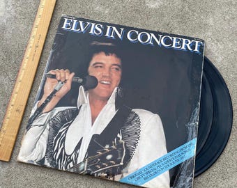 May include: A black vinyl record album cover featuring a photo of Elvis Presley in concert. The album title is "Elvis in Concert" and the text below the photo reads "Original Soundtrack Recording from the CBS-TV Special Plus Additional Songs Recorded on Tour June, 1977."