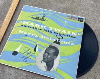 May include: A vintage vinyl record album cover featuring a portrait of Harry Belafonte, a black and white illustration of a steamboat, and the text "Mark Twain" and "other folk favorites". The album cover is blue, green, and white with a black and white record on top.