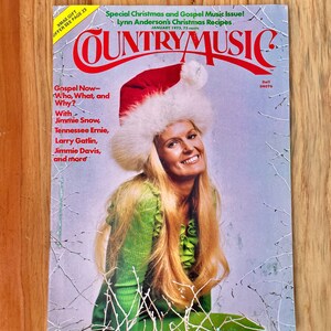 May include: A vintage Country Music magazine cover featuring Lynn Anderson wearing a white fur-trimmed Santa hat and a green sweater. The magazine cover is titled "Country Music" and features the text "Special Christmas and Gospel Music Issue! Lynn Anderson's Christmas Recipes." The magazine cover also features the text "Gospel Now - Who, What, and Why?" and lists several artists including Jimmie Snow, Tennessee Ernie, Larry Gatlin, Jimmie Davis, and more.