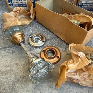 Peut inclure: Ensemble de salle de bain tubulaire Hampton Russwin vintage. L'ensemble comprend un bouton de porte en verre transparent, des accessoires en laiton et argent, et des boîtes en carton. Les boîtes sont étiquetées avec le nom de la marque et les informations sur le produit.