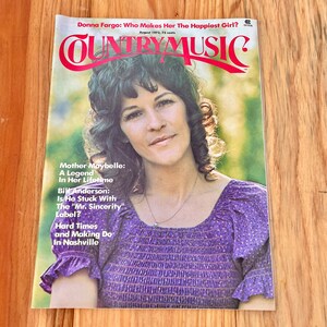 May include: A vintage Country Music magazine cover from August 1973 featuring Donna Fargo, a country music singer. The cover features a close-up photo of Donna Fargo in a purple and white patterned blouse. The magazine title is "Country Music" in red letters.