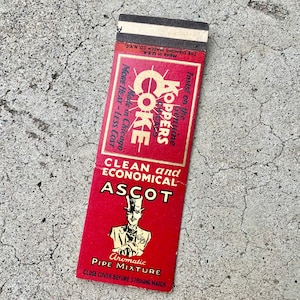 May include: A red and white matchbook for Koppers Coke Aromatic Pipe Mixture. The matchbook has the text "Insist on the Genuine Koppers Coke" and "More Heat - Less Cost" on the front. The back of the matchbook has a drawing of a man in a top hat and the text "Clean and Economical Ascot Aromatic Pipe Mixture. Close cover before striking match."