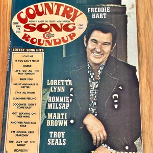 May include: A vintage magazine cover featuring a photo of country music singer Freddie Hart. The cover is titled "Country Song Roundup" and features a list of popular country music artists and songs from March 1974.