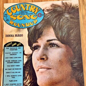 May include: A vintage magazine cover featuring Donna Fargo, a country music singer. The cover is yellow and blue with the title "Country Song Roundup" and a list of her latest song hits.