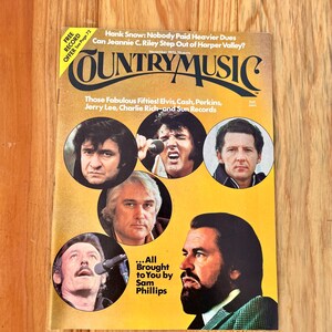 May include: A vintage Country Music magazine cover featuring a yellow background with the title "Country Music" in bold, black letters. The cover features five musicians in circular frames: Elvis Presley, Johnny Cash, Jerry Lee Lewis, Hank Snow, and Charlie Rich. The text below the title reads "Those Fabulous Fifties! Elvis, Cash, Perkins, Jerry Lee, Charlie Rich-and Sun Records." The text at the bottom of the cover reads "...All Brought to You by Sam Phillips."