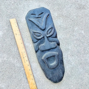 May include: A dark wood carved mask with a fierce expression. The mask has a wide mouth, large eyes, and a prominent nose. The mask is approximately 18 inches tall.