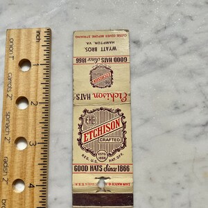 Puede incluir: Una caja de cerillas vintage que anuncia los sombreros Etchison, elaborados desde 1866. La caja de cerillas es roja, blanca y negra con un logotipo dorado. El texto dice "Etchison Hats Since 1866" y "Wyatt Bros. Hampton, VA."