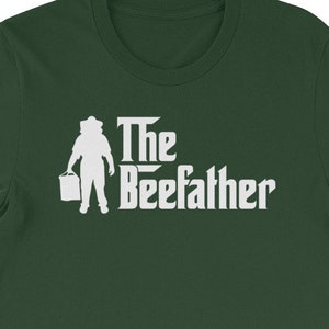 Może przedstawiać: Zielony T-shirt z białym siluetem osoby niosącej wiadro i napisem "The Beefather" nadrukowanym z przodu.