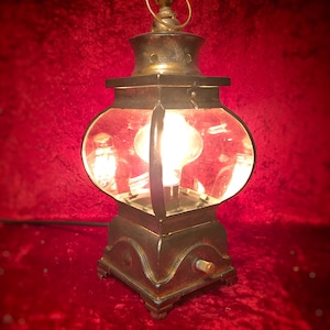May include: A vintage-style metal lantern with a clear glass globe and a light bulb inside. The lantern has a dark brown finish and a decorative top with a ring.