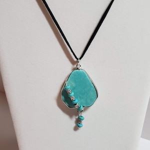 May include: A turquoise stone pendant necklace with a silver wire wrap and turquoise beads hanging from the bottom. The necklace is on a black suede cord.