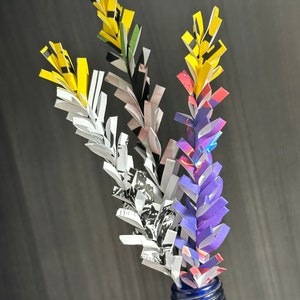 May include: A bouquet of paper flowers in a blue glass bottle. The flowers are made from strips of paper in yellow, black, white, purple, and pink.