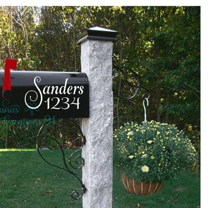 May include: Black mailbox with a white vinyl decal that says "Sanders 1234" with a decorative swirl. The mailbox is mounted on a gray stone post.