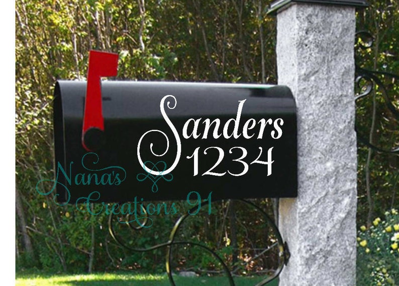 May include: A black mailbox with a white vinyl decal that says "Sanders 1234" in a cursive font. The mailbox is mounted to a gray stone post.