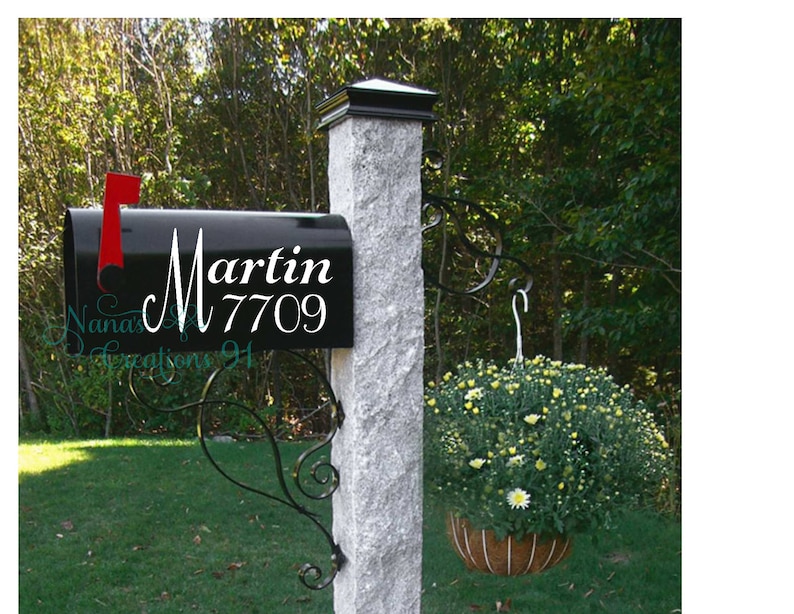 May include: A black mailbox with a white vinyl decal that says "Martin 7709". The mailbox is mounted on a gray stone post with a decorative metal bracket.