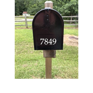 May include: Black mailbox with a white number 7849 on the front. The mailbox is mounted on a wooden post.