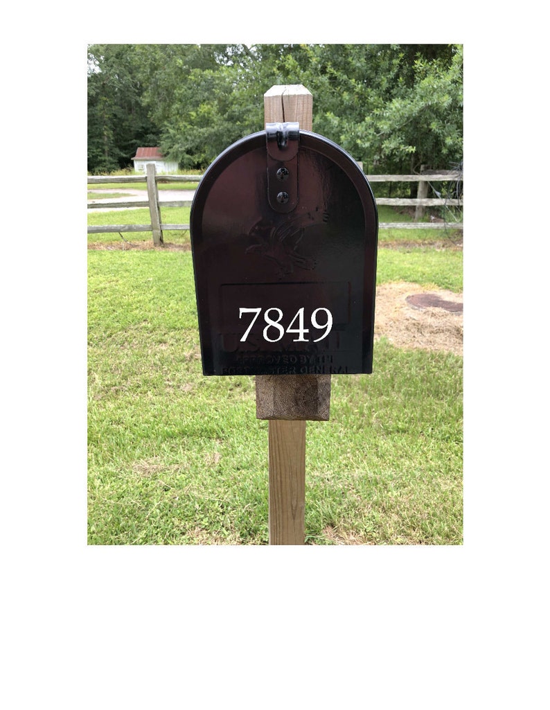 May include: Black mailbox with a white number 7849 on the front. The mailbox is mounted on a wooden post.