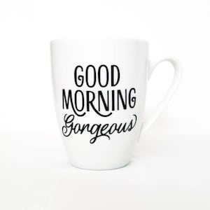 May include: White ceramic coffee mug with black text that reads "Good Morning Gorgeous".