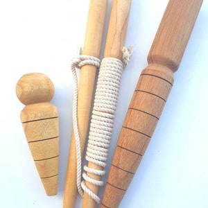 May include: Three wooden garden tools, two are long and thin with a rope wrapped around them, and one is shorter and thicker with a rounded top. The tools are made of light brown wood and have a natural finish.