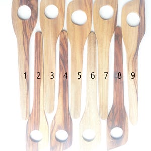 Peut inclure: Neuf spatules de cuisine en bois avec un trou dans le manche. Les spatules sont numérotées de 1 à 9.