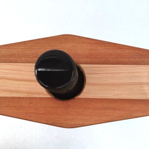 May include: A wooden wine rack with two suction cups for holding wine glasses. The rack is made of light and dark wood and has a diamond shape.