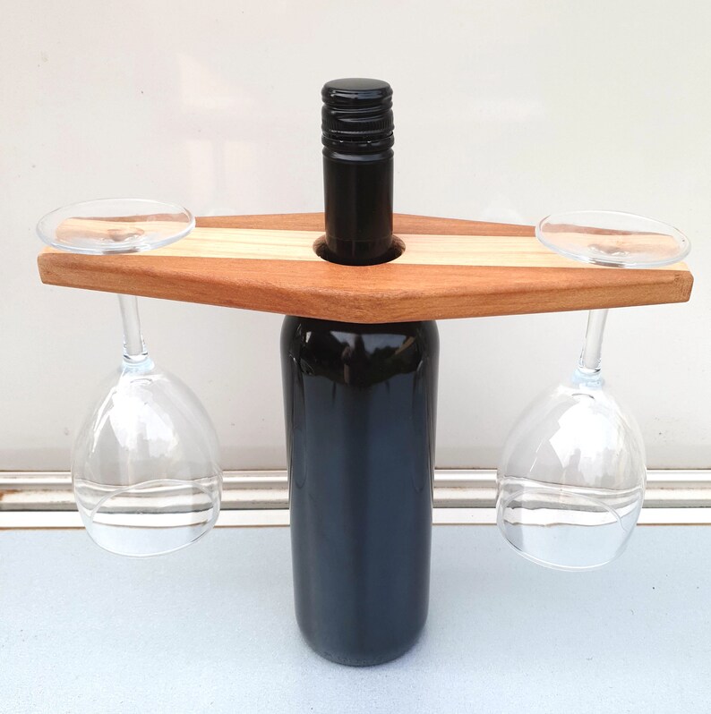 May include: Wooden wine bottle and glass holder with a natural wood finish. The holder has two slots for glasses and a center hole for a bottle.