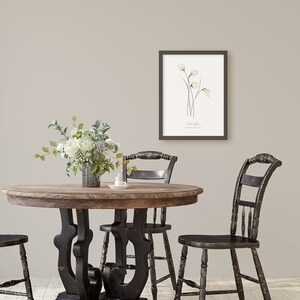 May include: A rustic wooden table with black painted legs and a black painted top. There are three black chairs around the table. A vase with white flowers sits on the table. A framed botanical print of white flowers hangs on the wall behind the table.