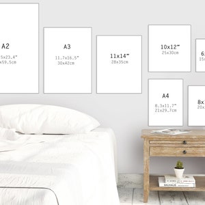 May include: A white wall with six different sized white frames, each with a black text label indicating the size of the frame in inches and centimeters. The frames are arranged in a staggered pattern, with the largest frame at the top left and the smallest frame at the bottom right. The frames are all empty, and the wall is a light gray color.