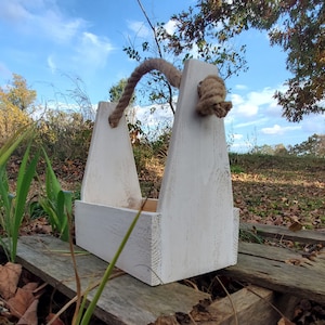 May include: White wooden bottle carrier with a rope handle. The carrier has a distressed white paint finish and is perfect for carrying six bottles of wine or beer.