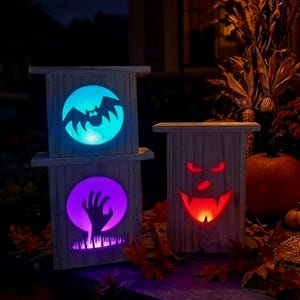 May include: Three rectangular wooden lanterns with cutouts. The top left lantern features a blue bat silhouette, the bottom left shows a purple hand reaching up, and the right lantern displays a red glowing face with sharp fangs and eyes.