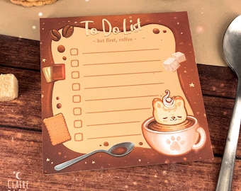 Puede incluir: Un bloc de notas de tareas pendientes marrón con un lindo gato de dibujos animados en una taza de café. El bloc de notas tiene un fondo marrón con estrellas blancas y el texto "To Do List - but first, coffee -" en la parte superior.