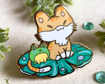 Pin doré de petit chat sur un nénuphar, accompagné de son ami grenouille