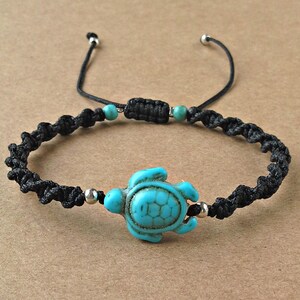 Op de afbeelding: Een zwarte gevlochten armband met een turquoise schildpadbedel en zilveren kralen.