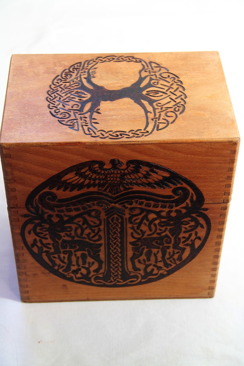 Peut inclure: Une bo&icirc;te en bois avec un motif de n&oelig;ud celtique sur le dessus et un motif d'arbre de vie sur le devant. La bo&icirc;te est en bois brun clair et a une teinture brun fonc&eacute;.