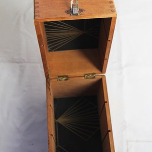 Peut inclure: Une bo&icirc;te en bois ouverte avec un int&eacute;rieur noir et un motif g&eacute;om&eacute;trique dor&eacute;. La bo&icirc;te a un couvercle &agrave; charni&egrave;res avec un loquet en m&eacute;tal.