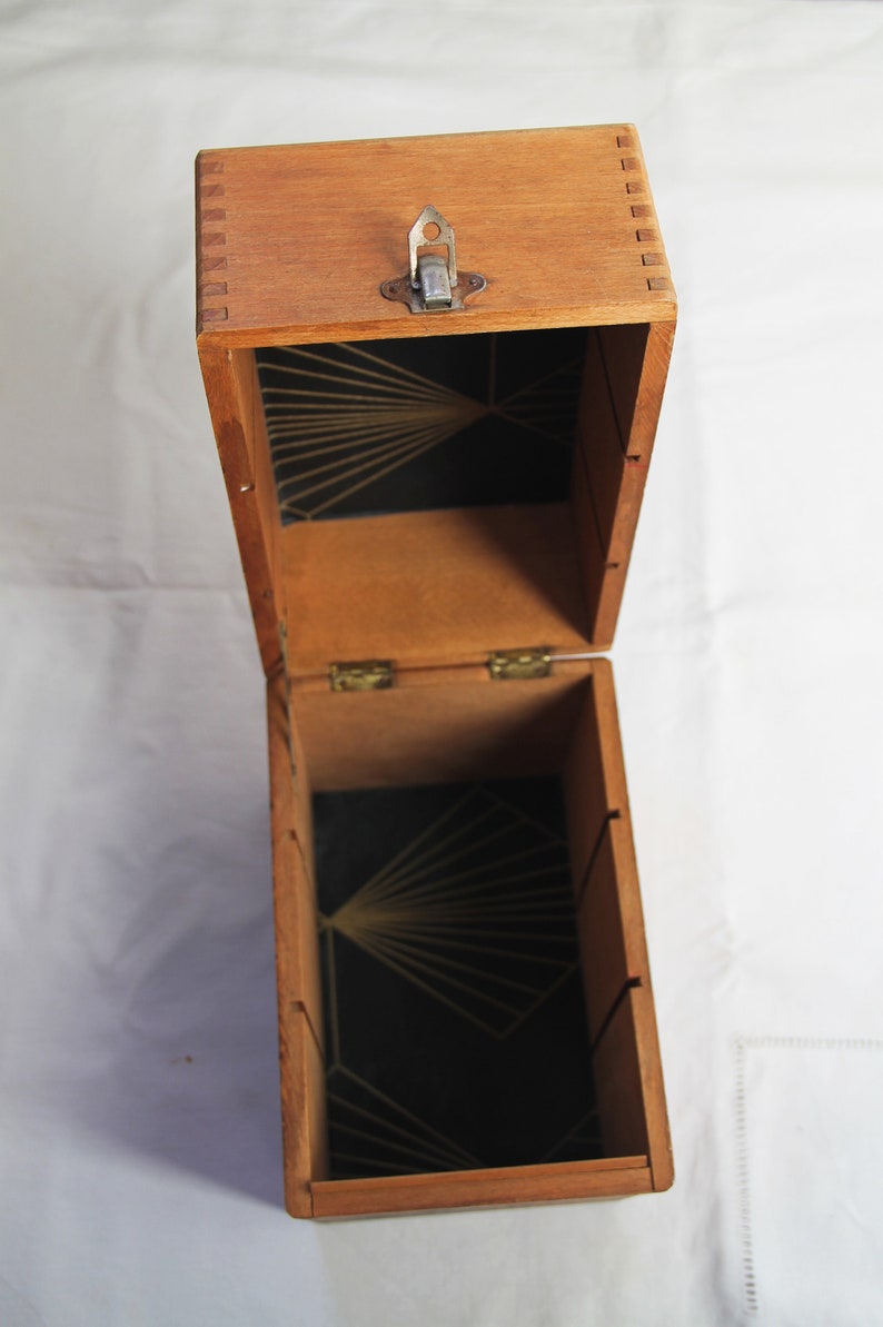 Peut inclure: Une bo&icirc;te en bois ouverte avec un int&eacute;rieur noir et un motif g&eacute;om&eacute;trique dor&eacute;. La bo&icirc;te a un couvercle &agrave; charni&egrave;res avec un loquet en m&eacute;tal.