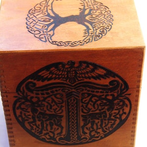 Peut inclure: Une bo&icirc;te en bois avec un motif de n&oelig;ud celtique sur le dessus et le dessous. Le motif repr&eacute;sente un arbre de vie avec un oiseau au sommet et un motif de n&oelig;ud stylis&eacute;.