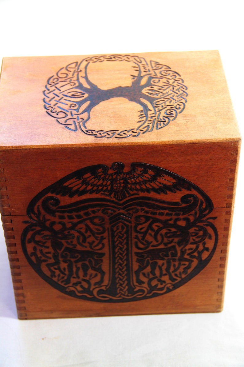 Peut inclure: Une bo&icirc;te en bois avec un motif de n&oelig;ud celtique sur le dessus et le dessous. Le motif repr&eacute;sente un arbre de vie avec un oiseau au sommet et un motif de n&oelig;ud stylis&eacute;.