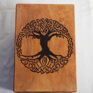Peut inclure: Une bo&icirc;te en bois avec un motif d'arbre de vie en n&oelig;uds celtiques br&ucirc;l&eacute; sur le dessus. La bo&icirc;te a un petit bouton en m&eacute;tal sur le devant.