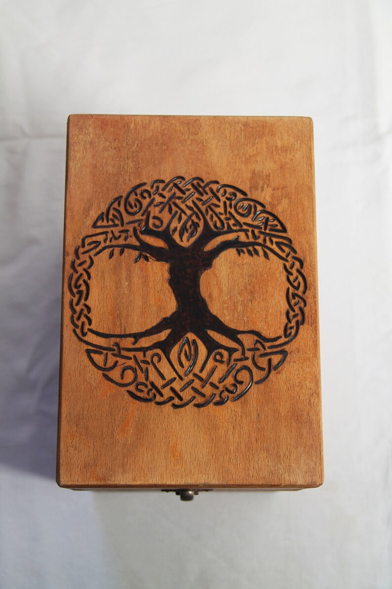 Peut inclure: Une bo&icirc;te en bois avec un motif d'arbre de vie en n&oelig;uds celtiques br&ucirc;l&eacute; sur le dessus. La bo&icirc;te a un petit bouton en m&eacute;tal sur le devant.