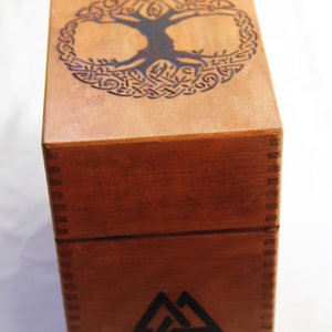 Peut inclure: Une bo&icirc;te en bois avec un motif d'arbre de vie sur le dessus et un symbole de triangle triple sur le devant.