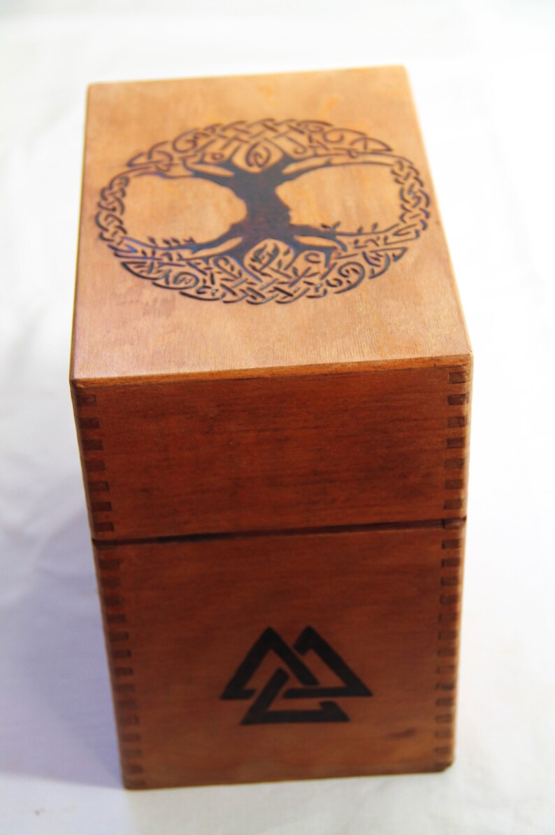 Peut inclure: Une bo&icirc;te en bois avec un motif d'arbre de vie sur le dessus et un symbole de triangle triple sur le devant.