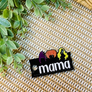 May include: Black acrylic keychain with three silhouettes of women with colorful hair and the word "mama" in white text. The text "www.bowdenhandmade.com" is printed below the word "mama".