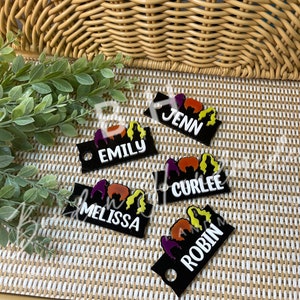 May include: Five black acrylic keychains with colorful cartoon images and white text. The names on the keychains are Jenn, Emily, Curlee, Melissa, and Robin.