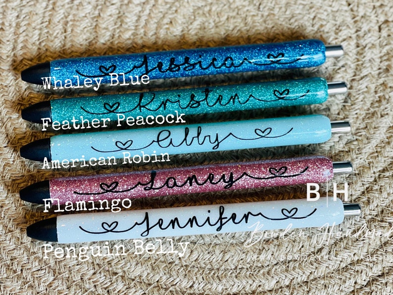 Puede incluir: Seis bol&iacute;grafos de purpurina con nombres escritos en ellos. Los bol&iacute;grafos son de los colores: azul whaley, pavo real de plumas, petirrojo americano, flamenco, vientre de ping&uuml;ino y azul claro. Los nombres en los bol&iacute;grafos son Jessica, Kristen, Abby, Janey, Jennifer, y el &uacute;ltimo bol&iacute;grafo tiene las iniciales BH.