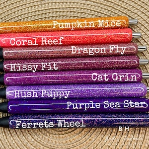 Puede incluir: Un conjunto de ocho bol&iacute;grafos con purpurina de diferentes colores y nombres impresos. Los nombres son: Pumpkin Mice, Coral Reef, Dragon Fly, Hissy Fit, Cat Grin, Hush Puppy, Purple Sea Star y Ferrets Wheel.